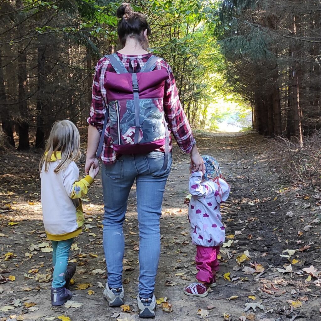 žena drží za ruce dvě holky, nese rolovací batoh