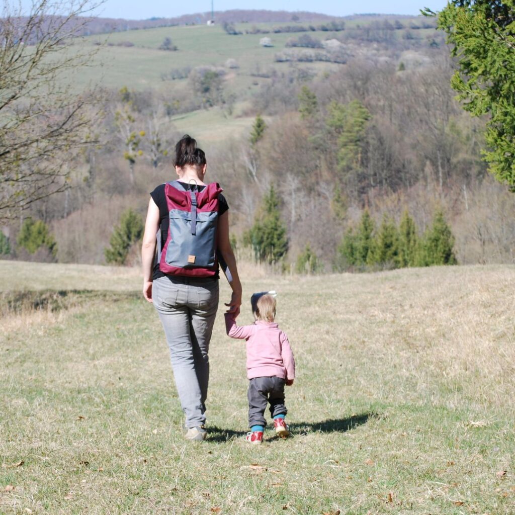 žena drží za ruku malé dítě, na zádech nese sportovní batoh ušitý podle jejího střihu na batoh